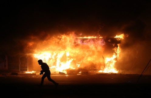 A photographer runs by a burning building during a demonstration on November 25, 2014 in Ferguson, Missouri.