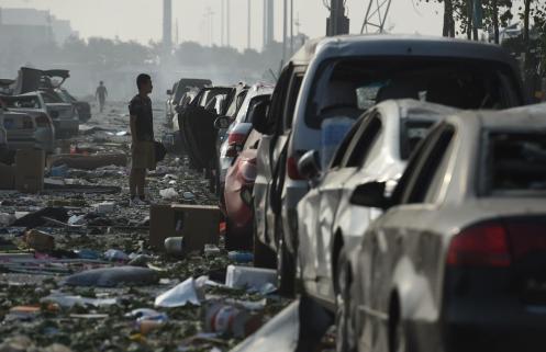 A man looks at a row of damaged cars outside a damaged residential building. (Greg Baker)