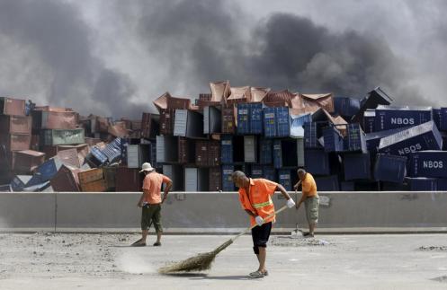 Workers clean debris form the road near the explosion site, where stacks of shipping containers had crumbled. (Jason Lee)